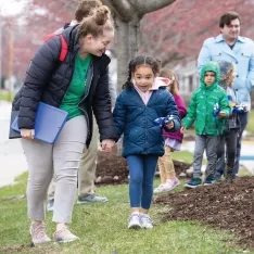 A woman and elementary student walking down a sidewalk outside their school.